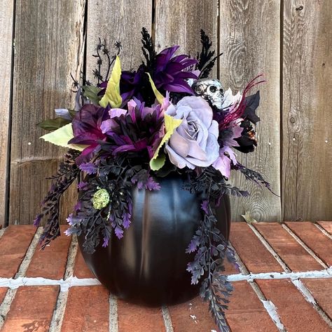 This  flower arrangement features all the things that make Halloween fun and  beautiful.  The black artificial pumpkin has the lid carved out and attached to the back of the arrangement.  The center is filled with flowers in the hues of gray, purple, black, and green.  Fun picks feature a silver skull, a purple and a green spider small spider web.  Black and purple feathery sprays and glittery berry sprays complete this arrangment   The pumpkin arrangement measures 15" in heigth and 12" at the widest part.   Item #FLR - 84 Halloween Flowers Bouquet, Spooky Flower Arrangements, Spooky Apartment, Halloween Flower Arrangements, Quince Planning, Halloween Floral Arrangements, Pumpkin Floral Arrangements, Green Spider, Tissue Paper Flowers Diy