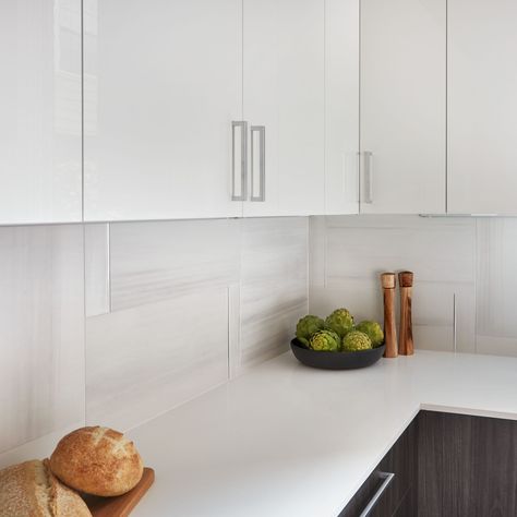 Creating a modern kitchen backsplash can feel daunting, but using a larger tile can be the perfect solution! This pattern with our Themar Bianco Lasa 12x24 porcelain tile adds a clean look to this ultra-modern space. https://www.arizonatile.com/en/products/recycled-material-content/themar Features Products: Themar Bianco Lasa and Absolute White Polished Quartz 12x24 Tile Backsplash Kitchen, 12x24 Backsplash Kitchen, White Tiles Kitchen, White Glossy Kitchen, Kitchen Ceiling Designs, Modern Kitchen Inspiration, Kitchen Budget, Porcelain Tiles Kitchen, Modern Kitchen Colours