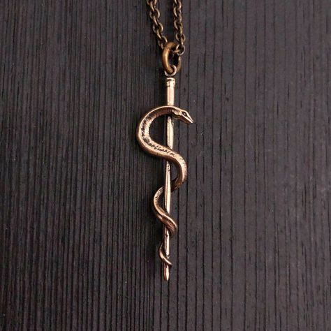 "This beautifully detailed Rod of Asclepius is an ancient Greek symbol associated with astrology and with healing the sick through medicine. It consists of a serpent entwined around a staff. Asclepius, the son of Apollo, was practitioner of medicine in ancient Greek mythology. This handmade piece is cast in solid bronze, oxidized in recesses to enhance the fines detail of this 1.75\" long pendant. It will arrive in a branded \"Moon Raven Designs\" gift box ready to present to a graduating nursin Son Of Apollo, Ancient Greek Symbols, Rod Of Asclepius, Greek Mythology Jewelry, Zara Necklace, Raven Jewelry, Mythology Jewelry, Ancient Greek Mythology, Greek Symbol