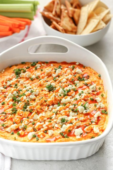 A white baking dish filled with creamy buffalo chicken dip topped with blue cheese, chives, and buffalo sauce. A bowl of chips and a plate with celery and carrot sticks in the background. Creamy Buffalo Chicken Dip, Buffalo Chicken Cups, Creamy Buffalo Chicken, Live Well Bake Often, Pregnancy Recipes, Enchilada Sauce Easy, Chicken Dip Recipe, Buffalo Chicken Dip Recipe, Easy To Cook Meals