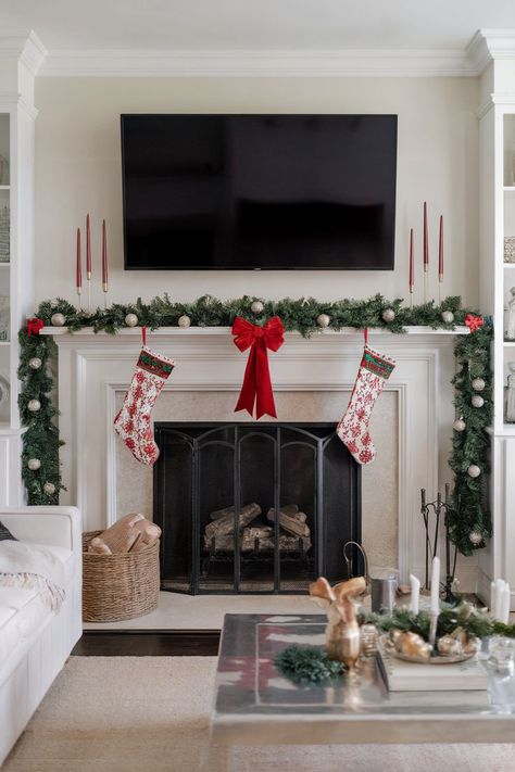 A fireplace decorated for Christmas with garland and red accents, complemented by a TV mounted above for a modern holiday setup. Fireplace Christmas Decorations With Tv, Fireplace Christmas Decor Ideas, Tv Christmas Decor, Fireplace Christmas Decorations, Fireplace Christmas Decor, Christmas Fireplace Decor Ideas, Fireplace Decor Christmas, Festive Fireplace, Fireplace Decor Ideas