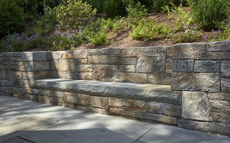 Ashlar style stonewalls retain a planted hillside. Beautiful rock faced bluestone slab provides patio seating at this outdoor living room. Personal favorite! #stonewalls #stonemasonry #hardscape #patio #landscapedesign #gardenwalls #landscapeideas #stonebench #outdoorliving #outdoorlivingspace #garden Steep Retaining Wall, Bench Built Into Hillside, Bluestone Retaining Wall, Retaining Wall Bench Seating, Retaining Wall With Seating, Retaining Wall Bench, Natural Stone Garden, Retaining Wall Patio, Hardscape Patio