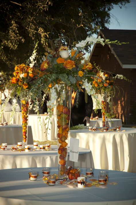 Table Centerpieces    - Tall tapered glass vases filled with dried flowers in fall colors  - Arrangement of orange roses, gerbera daisies, greenery, curly willow, and hanging white flowers Orange Centerpieces, Floristry Design, Table Arrangements Wedding, Autumn Wedding Reception, Fall Table Centerpieces, Beautiful Outdoor Wedding, Wedding Reception Flowers, Flower Vase Arrangements, Tall Vase