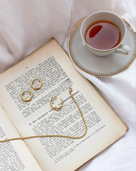 Gold jewelry laying on book with cup of tea Accessories Shoot Ideas, Gold Jewelry Photography Ideas, Aesthetic Jewelry Pictures, Jewellery Photoshoot Ideas At Home, Accessories Photography Ideas Photo Shoot, Flat Lay Jewelry, Earings Photography Idea, Winter Jewelry Photoshoot, Jwellery Photoshoot Idea