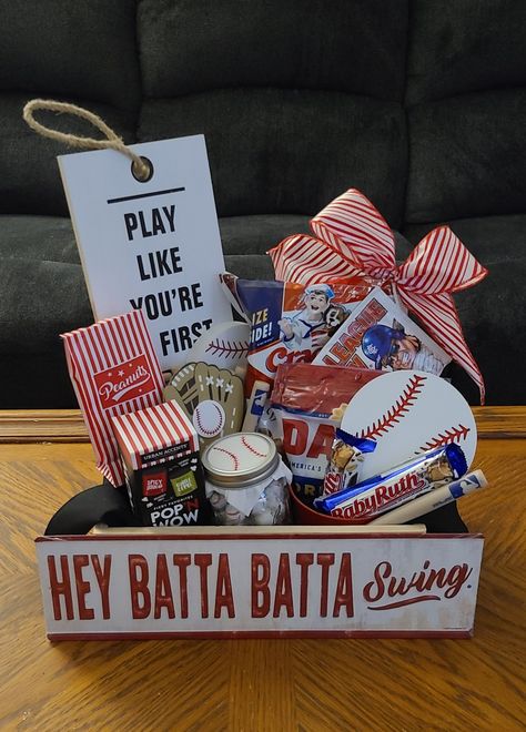 Baseball basket: Cracker Jacks, David sunflower seeds, Big League Chew, tin bucket for shells, Baby Ruth bars, MLB baseball bat pens, MLB cup(party city) table decor wooden baseball, wood sign, tin sign, Planters Peanuts inside peanut bags, Mason jar with candies, tissue paper with baseball stitching drawn on, popcorn kernels, crate & tin sign from Hobby Lobby, pre-painted wooden baseball & mitt from Hobby Lobby made into magnets. Add a bow if desired. Baseball Silent Auction Basket, Baseball Themed Baskets For Raffles, Baseball Theme Gift Basket, Baseball Favors For Team, Baseball Themed Basket, Baseball Senior Night Basket Ideas, Senior Night Buckets, Baseball Auction Basket Ideas, Baseball Coach Gift Basket