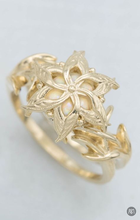 This gold engagement ring was inspired by Nenya, an elvish ring of power worn by Galadriel in the Lord of the Rings. The design we created for this customer sets a white opal under yellow gold flower detail to blend her love for the trilogy and for the unique look of opal. The unique styling of this design also provides a layer of protection for the softer opal. Nenya Ring Galadriel, Elvish Wedding Rings, Lord Of The Rings Wedding Ring, Lord Of The Rings Engagement Ring, Nenya Ring, Galadriel Ring, Galadriel Rings Of Power, Lord Of The Rings Jewelry, Nerdy Engagement Rings