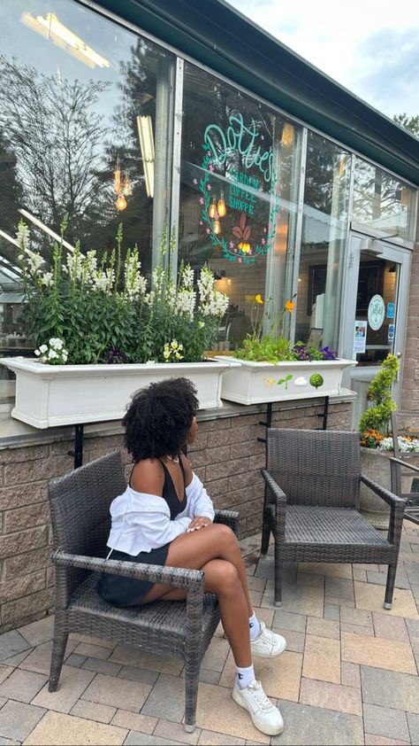 black girl sitting in dark chair in front of white flowers, greenery, plants, white jacket, black skirt, white shoes, outdoors, patio furniture, window art Nursery Greenery, Tennis Skirt Style, Outdoors Photoshoot, Outfit Basics, Hair Spring, Greenery Flowers, Black Tennis Skirt, Aesthetic Plants, Sitting Pose