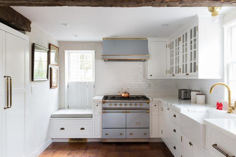 Welcoming white kitchen is equipped with a farmhouse sink paired with a brass gooseneck faucet mounted to a honed white marble countertop in front of a window and above white shaker cabinets adorned with oil rubbed bronze pulls. Nantucket Interior Design, Lacanche Range, Spice Cabinets, Subway Backsplash, White Shaker Cabinets, Low Ceilings, Wood Beam Ceiling, Wood Ceiling, White Marble Countertops