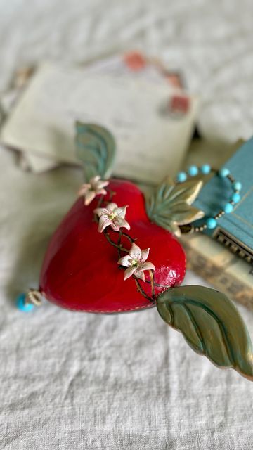 Carrie Ann Jackson on Instagram: "“The Lily Heart” Sacred Heart Ornament. (Sold) ♥️🪷 This #Lily #heart is part of a #commission for a celebration of life. Each heart went to a different person, this one went to someone very close to the one being remembered. For this #customorder I worked closely with my client to learn about the the heart of the person being honored. These two shared a love of shopping (esp. #homegoods) and a sharp sense of humor. The last line “gotta go someone’s on the oth Air Dry Clay Sacred Heart, Clay Sacred Heart, Mexican Folk Art Decor, Artisan Gifts, Sacred Hearts, Different Person, 2023 Art, Artisan Gift, Heart Ornament