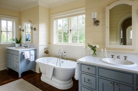 Cream and blue cottage master bathroom colors offer a relaxing vibe starting with a roll top vintage style bathtub under a window between blue vanities with white quartz countertops and satin nickel vintage cross handle faucets. Bathtub Window, Blue Bathtub, Master Suite Remodel, Bathroom Blue, Shiplap Bathroom, Rustic Bathroom Vanities, Bathroom Color Schemes, Cottage Bathroom, Diy Bathroom Remodel