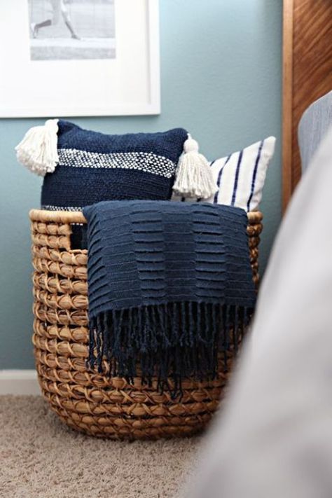 A wicker catch-all adds a rustic touch to a bedroom and creates an instant way to store pillows with ease. If you get one that's big enough, you can add throw blankets to the basket as well. Click through for more on this and other bedroom throw pillow storage ideas. Bedroom Throw, Pillow Storage, Throw Pillows Bedroom, Teen Boy Bedroom, Spare Bedroom, Wicker Basket, Blue Bedroom, Boy's Bedroom, Organization Bedroom