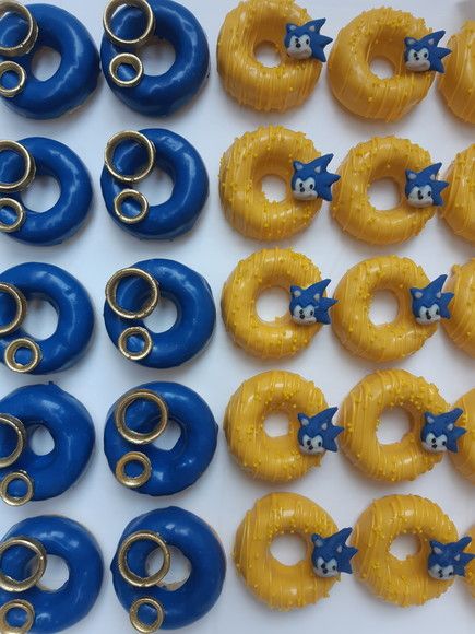 Mini Donuts Personalizados no tema do Sonic.    **FOTO de nossa autoria.    Valor do anúncio por unidade sendo 20 unidades o mínimo:    10 Mini Donuts Amarelo  - Listras Amarelas  - Miçangas amarelas  - Rostinho do Sonic    10 Donuts Azul esculto  - 2 aneis cada Mini Donuts    (Produzimos os apliques com chocolate.)    - Mini Donuts avulsos em caixa de transporte.  - Massa de Baunilha com Cobertura de Chocolate.  - TAMANHO: 6,5cm    (Nossos Mini Donuts não possuem recheio)    - Validade: 3 Dias Sonic Party, Donut Bar, Cake Day, Mini Donuts, Baby Birthday, Donuts, Sonic, Birthday, Design