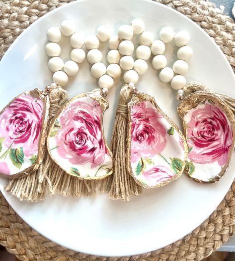 "Set of eight oyster shell napkin rings, with an elegant pink rose tropical Coastal preppy shell design.   These napkin rings make an elegant addition to a beautiful coastal or any dining experience and tabletop decor. When given as a wine bottle or champagne bottle charm, it becomes a unique, one-of-a-kind gift. Great for use at Thanksgiving, a dinner party or over the Holidays. The bowl of the oyster shell has been sealed and can be cleaned with a damp cloth. The edges of each shell were finished with a liquid gold leaf paint. The shells are approximately 2-3\" tall and have been strung with natural wood beads on jute to create the loop. Due to the natural variations of the oyster shells, the exact size of the shell and details within the print pattern will vary. How special is that! If Oyster Shell Napkin Rings, Chinoiserie Paintings, Beachy Christmas Tree, Shell Napkin Rings, Broken China Crafts, Liquid Gold Leaf, Coastal Preppy, Napkin Rings Wedding, China Crafts