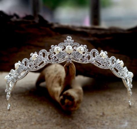 Adorned with iridescent pearls and intricately faceted clear rhinestones that work their way across the band in a swirly pattern, this delicate tiara can complete the most sophisticated of bridal looks. Cast in lightweight alloy and rhodium plated for a flawless finish, the headband measures 1.25" at the tallest point (approx. 3.2cm) and 5.5" across (approx. 14cm). Two small loops at each end make it easy to attach to your hair with bobby pins. Its incredible sparkle coordinates with any color w Real Tiaras, Pearl Tiara Wedding, Pearl Tiara, Beautiful Tiaras, Hair Accessories Pearl, Rhinestone Tiara, Iridescent Pearl, Princess Tiara, Rhinestone Bridal