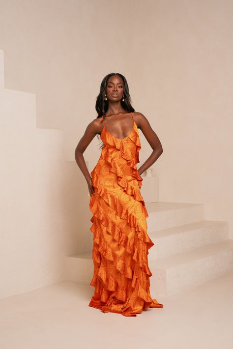 Turn heads in the stunning Iza Orange Ruffle Maxi Dress, designed to capture the essence of bold elegance. The vibrant orange hue radiates warmth and energy, while the cascading ruffles add movement and a touch of drama to every step. Perfect for resort getaways or special events, this statement dress features a flattering silhouette with a flowing, floor-length skirt that exudes femininity and grace. Whether you're attending a formal occasion or a sunset soirée, the Ruffle Maxi Dress ensures you'll shine with confidence and style. Printed silk feel ruffle maxi dress 95% polyester  5% spandex Hand wash Rust Orange Dresses, Wedding Guest Orange Dress, Orange Wedding Dress Guest, Puerto Rico Wedding Guest Dress, Orange Formal Dress Long, Burnt Orange Wedding Guest Dress, Apricot Bridesmaid Dresses, Orange Graduation Dress, Colorful Wedding Guest Dress