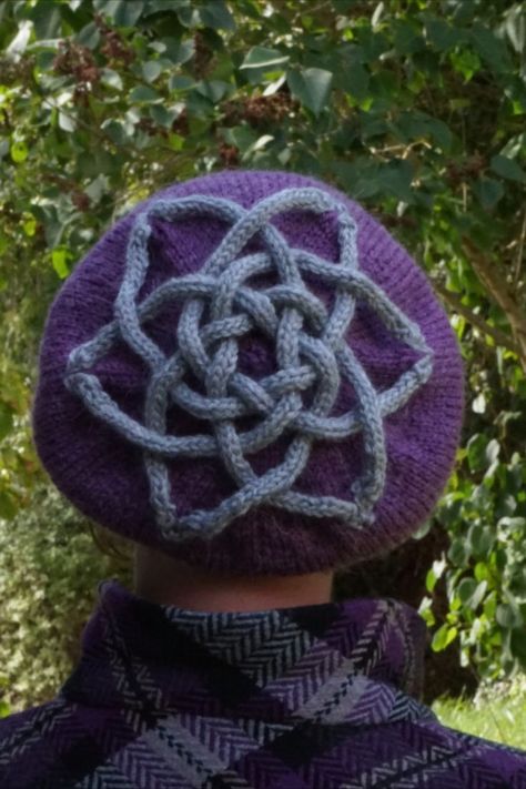 A woman wears a purple coat and hat.  Her back is to the camera, and the crown of the beret hat has an intricate celtic knot worked in silver Tam Hat, Beret Pattern, Hat Knitting Pattern, Hat Knitting, I Cord, Bramble, Hat Knitting Patterns, Worsted Weight Yarn, Worsted Weight