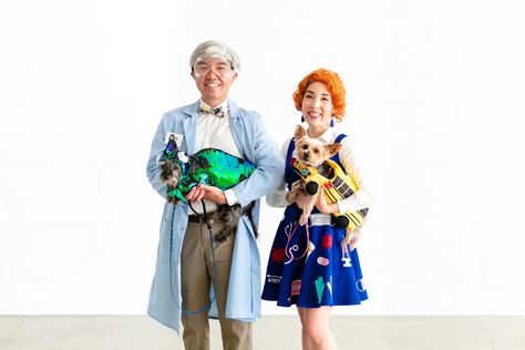 Photo of couple and two dogs dressed in costume. Asian man is dressed as Bill Nye in a blue lab coat, tie and white wig. Asian woman is dressed as Ms. Frizzle with orange curly hair and printed dress. The dogs are dressed as Liz the chameleon and the Magic School Bus. Ms Frizzle Dress, Ms Frizzle Costume, Magic School Bus Characters, Ms Frizzle, Miss Frizzle, Bill Nye, Magic School Bus, Magic School, Family Costumes