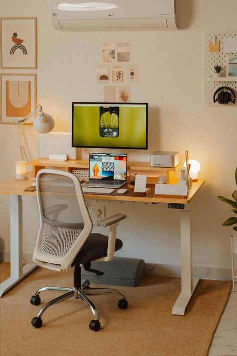 A cozy home office setup with a wooden desk, a white ergonomic chair, and walls adorned with modern art prints. The desk is neatly organized with a computer monitor, a laptop, and various creative tools, illuminated by a soft desk lamp and natural light. Working From Home Aesthetic, Workspace Studio, Desk Layout, Cozy Home Office, Desk Inspiration, Aesthetic Space, Warm Lighting, Warm Home, Home Aesthetic