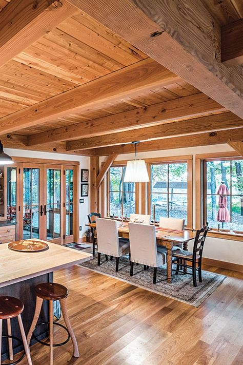 The connected open space on the 1,200 square-foot main level is filled with dining, living and kitchen areas. The Douglas fir posts and timbered ceilings establish a sense of contentment and comfort, while the abundant natural light gives it levity and space to breathe. The kitchen’s perimeter counters are capped with Corian while the center island is topped with silky maple. Photography by Scott Hemenway. Timber Frame Kitchens, Douglas Fir Walls, Timber Frame House Interior, Timber Ceilings Interior, Timber Frame Interior Design, Timber Frame Home Interiors, Barndo Interior, Timber Interior, Cabin Walls