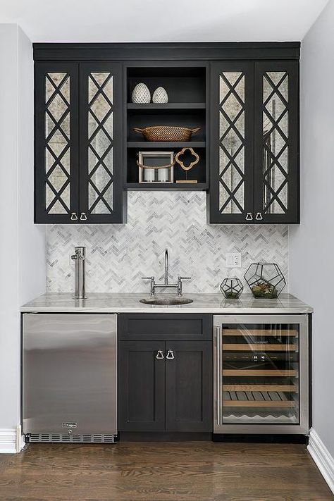 Black mirrored cabinets flank stacked black shelves mounted above marble herringbone backsplash tiles lining a gray stone countertop. Herringbone Tiles, Herringbone Tile Backsplash, Speakeasy Decor, Dining Room Built In, Marble Herringbone, Home Wet Bar, Home Bar Rooms, Pantry Cabinets, Bar Basement