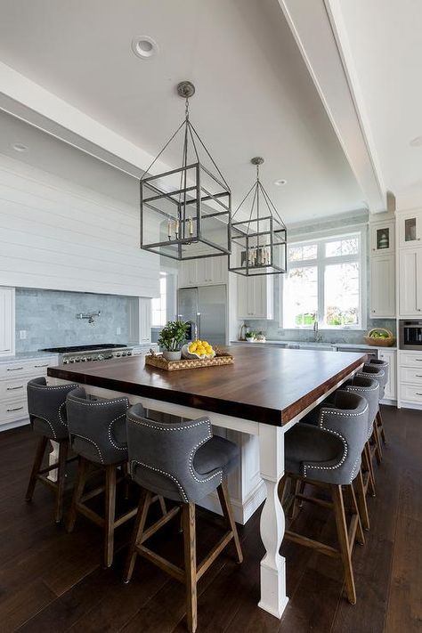 Two glass and iron lanterns hang from a tray ceiling over an oversized white island seating gray low wingback counter stools at a butcher block countertop. Lighting Ideas For Low Ceilings, Ideas For Low Ceilings, Kitchen Lighting Ideas For Low Ceilings, Kitchen Coastal, Best Kitchen Lighting, Wood Countertops Kitchen, Cheap Kitchen Decor, Kitchen Lighting Ideas, Brown Floor