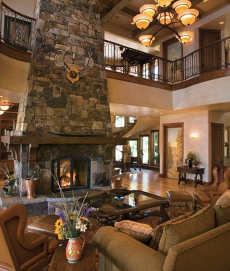 Great room featuring two-story stone fireplace; second-floor balcony overlooking great room and large chandelier Fireplace Separating Living And Dining, Stone Fireplaces Floor To Ceiling, Rustic House Living Room, 2 Story Fireplace Ideas, Stone Fireplace Floor To Ceiling, Two Way Fireplace, Large Stone Fireplace, Big Fireplace, Grand Fireplace