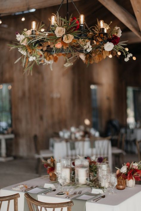 Dress up your chandelier with florals and greenery to tie in the romantic elements of your decor! For more lighting inspiration, check out our website! #WeddingLights #RusticWeddingDecor #Floral #Greenery #Chandelier #SweetheartTable #EventLights #Wedding2022 Autumn Chandelier Decor, Fall Floral Chandelier Wedding, Fall Chandelier Decorations, Fall Wedding Lighting, Chandelier With Greenery, Reception Lighting Ideas, Greenery Chandelier, Floral Chandelier Wedding, Chandelier Decorations