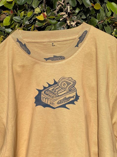 Printed with hand carved linocut/block print stamps. Each piece is unique and imperfect and printed at my home studio in Los Angeles. No digital printing or drop shipping here! This shirt features tinned fish as its main design with a can of sardines in navy blue on the front of the shirt. It also features a collar and sleeve detail front and back with sardines encircling:) This would be a great shirt to wear on a hike, to the farmer's market or just lounging around. Maybe even as a gift for you Design On Clothes Art, Cool Printed Shirts, Linocut Tee Shirt, Bleach Graphic Tee, Shirt Stamp Ideas, Block Printing Stamps, Retro Graphic Tshirt, Screen Print Clothes, Block Printed Clothes