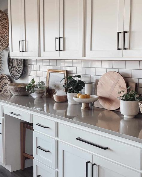 White farmhouse kitchen cabinets are finished with black pulls and a gray countertop. The countertop is styled with white and wood kitchen decor perched in front of a white subway tile backsplash. Light Grey Cabinets, White Kitchen Counters, Gray Countertops, White Subway Tile Kitchen, White Tile Kitchen Backsplash, White Shaker Kitchen Cabinets, Light Gray Cabinets, White Tile Backsplash, White Subway Tile Backsplash