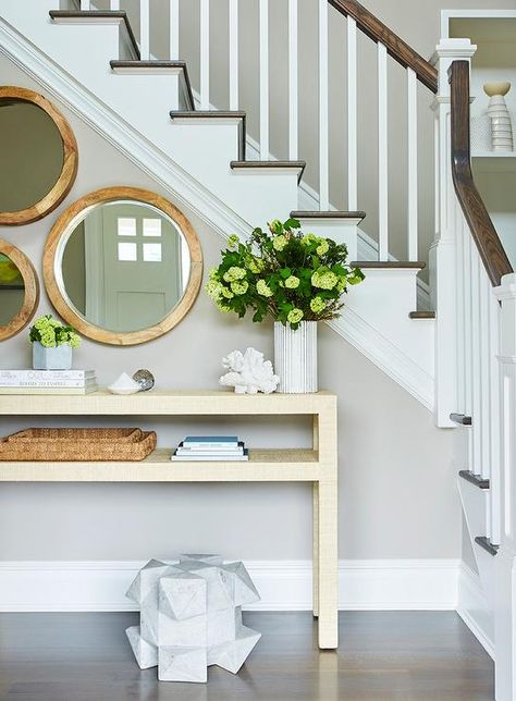 A staircase wall is lined with round staggered mirrors placed over a gold raffia console table with shelf styled elegantly. Staircase Wall, Console Table Hallway, Modern Entryway, Foyer Design, Beach House Design, Plywood Furniture, Under Stairs, Coffee Table Design, Decorating On A Budget