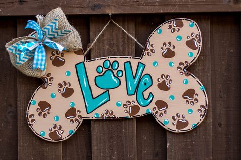 "Dog lovers welcome!  Welcome friends and family to your home with this hand painted wooden door hanger! This dog door hanger features a dog bone painted with the word \"LOVE\" and surrounded with pawprints.  The O in Love is also a paw print.  Any color combination that you prefer can be painted.  A large bow is on top of the dog bone door hanger. This would make a perfect gift for a dog lover, dog groomer, or your vet! Let us know what colors you would like at checkout. This Valentine's Day do Dog Bone Door Hanger, Dog Door Hangers Wooden, Dog Door Hanger, Valentines Door, Pet Wreath, Yard Art Crafts, Paint Crafts, Valentines Door Hanger, Wooden Things