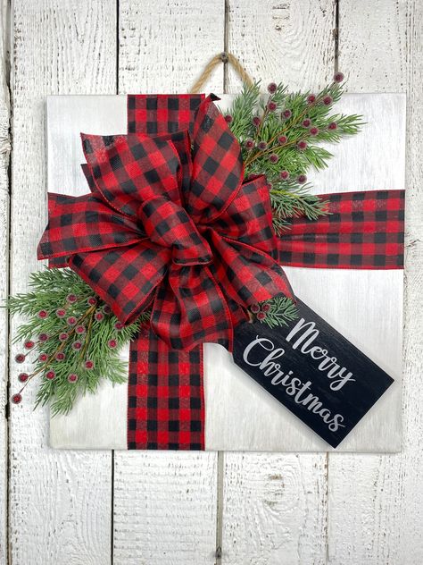 This Christmas gift door hanger is a unique piece, perfect for a door or wall in your home or place of business.  Give as a housewarming or hostess gift, hang or lean over a mantel or on a shelf. This is also a great decor piece to fit between a storm/screen door because of its thickness. This is made on an 18" wooden square (1/4" thick) which is painted and lightly sealed, looking like a Christmas present all wrapped up with a large messy bow, faux greenery and berries and a wooden gift tag messaging Merry Christmas.  Final measurements are approximately 19" and about 5" in depth, which includes the greenery and bow. This is best displayed indoors but if choosing to hang outside, please hang ONLY in a dry, well-covered area. Exposure to the elements will damage the door hanger and/or its Square Christmas Door Hanger, Christmas Door Hangers Diy, Christmas Door Hangers Wooden, Christmas Present Door, Square Door Hanger, Holiday Door Hangers, Present Door, Holiday Door Decor, Door Decor Christmas