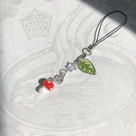 Red Mushroom Phone Charm This handmade phone charm is made with a leaf charm, an iridescent star bead, a silver spiral charm, and a glass mushroom charm. The length of this phone charm is about 4.5 inches. Mushroom Phone Charm, Mushroom Beads, Mushroom Keychain, Beaded Charms, Red Mushroom, Diy Jewelry Unique, Diy Bracelets Patterns, Phone Charms, Handmade Jewelry Tutorials