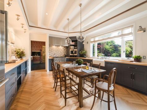 A spacious farmhouse table is the focal point of this dreamy cottage kitchen. Gray cabinets stretch across each side of the kitchen, providing plenty of storage space. The white vaulted ceiling and globe pendant lights add to the elegance. Galley Kitchen With Table, Kitchen With Table In Middle, Kitchen With Table, Kitchen Booths, Hgtv Kitchens, Kitchen Design Styles, Galley Kitchen Remodel, Gray And White Kitchen, Small Kitchen Tables