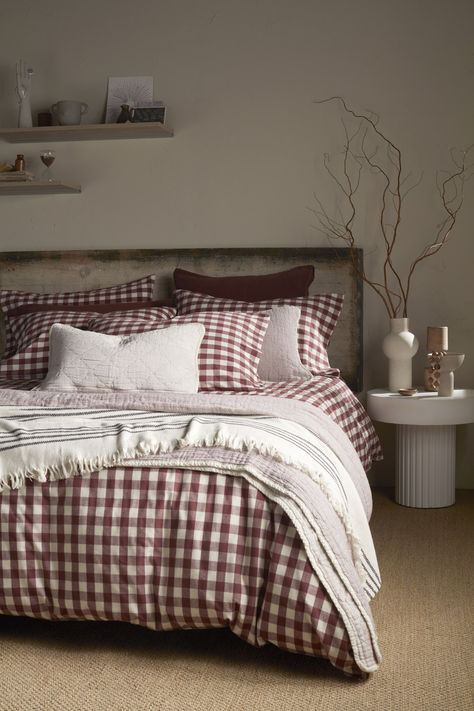 A cozy bed styled with burgundy gingham bedding, layered with textured neutral cushions and a striped throw. The room features earthy decor accents, including dried branches and a rustic headboard, creating a warm, autumnal, and rustic bedroom look. Bedroom Autumn, Gingham Bedding, Bed Setup, Teal Bedding, Baby Cot Bedding, Cosy Bed, 100 Cotton Duvet Covers, Organic Cotton Bedding, Yellow Bedding