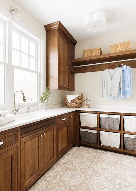 Tan mosaic floor tiles complement brown wood laundry room cabinets fitted with polished nickel hardware and a white quartz countertop, while a sink with a polished nickel gooseneck faucet is positioned under a window. Brown Laundry Room, Transitional Laundry Room, Bria Hammel Interiors, Bria Hammel, Laundry Room Colors, Millwork Wall, White Laundry Rooms, White Laundry, Laundry Room Shelves