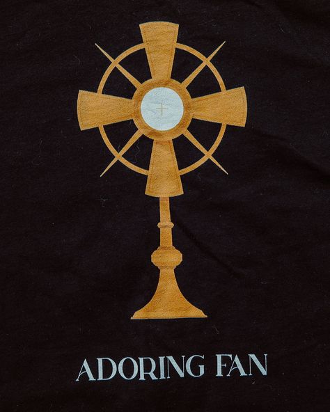 Y'all know I'm all for Catholic humor and this shirt was born of that adoration for humor and puns (there I go again...) Introducing "Adoring Fan" - a simple and SUPER Catholic tee. Beneath the glorious monstrance are the words "ADORING FAN", which has two meanings: 1) The wearer adores Jesus in the Eucharist and 2) The wearer also thinks that adoration is pretty spectacular Available in black, this unisex shirt is great to wear to holy hour, gift to priests or new Catholics, or anyone el... Holy Hour, Catholic Humor, Eucharistic Adoration, The Eucharist, Eucharist, First Communion, My Vibe, Unisex Shirt, Design Inspo