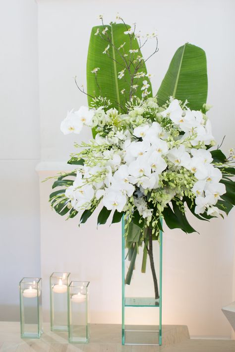 Phaleonopsis orchids and banana leaves help to create this fresh and beautiful altar arrangement Banana Leaves Wedding Decor, White Tropical Floral Arrangements, Bamboo Floral Arrangements, White Tropical Arrangement, Phaleonopsis Orchids, Orchid And Fern Arrangements, Hawaiian Centerpieces, Hawaiian Flower Arrangements, Florist Ideas