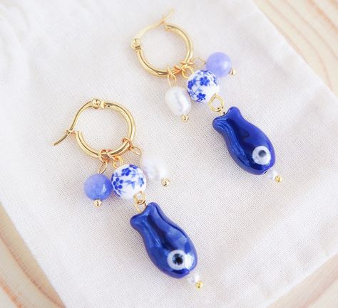 ༄ Handmade 𝙂𝙤𝙡𝙙 𝙎𝙖𝙧𝙙𝙞𝙣𝙚 𝘼𝙯𝙪𝙡𝙚𝙟𝙤 𝙋𝙚𝙖𝙧𝙡 earrings blend tradition with elegance. Inspired by the ocean and the historical culture of Portugal.🌊🐟🇵🇹 The dark blue ceramic 𝗦𝗮𝗿𝗱𝗶𝗻𝗲 𝗙𝗶𝘀𝗵 pendants honors Portugal’s coastal heritage and symbolizes resilience and prosperity.🐟 Combined with 𝗔𝗻𝗴𝗲𝗹𝗶𝘁𝗲 𝗴𝗲𝗺𝘀𝘁𝗼𝗻𝗲 beads, known for its calming properties, this bead reminds us of the calming ocean but also the colors of 𝗦𝗘𝗔 𝗕𝗬 𝗟𝗢𝗨.💙 The 𝗔𝘇𝘂𝗹𝗲𝗷𝗼 𝗧𝗶𝗹𝗲 ceramic bead inspired by Portugal’s iconic azulejos, these t... Sardine Fish, Ocean Inspired Jewelry, Seashell Earrings, By The Ocean, Ocean Inspired, Inspired Jewelry, Ocean Inspiration, Handmade Gold, Ceramic Beads