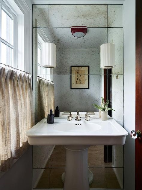 French pedestal sink sits on antiqued paneled mirrors lit by white sconces. Pedestal Sink With Oval Mirror, Pedestal Sink Vanity, Pedestal Vanity, Paneled Mirror, Classic Pedestal Sink, Vintage Pedestal Sink, Pedastal Sink, Small Bathroom Pedastal Sink With Wallpaper, Pedistal Sink