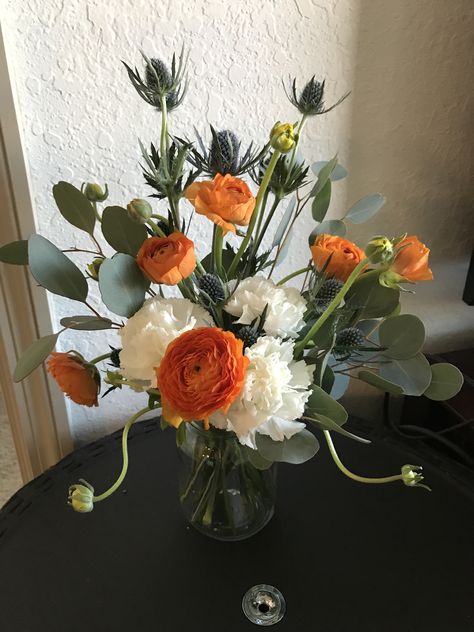 Fall flower arrangement: blue milk thistle,  orange ranunculus, carnations, eucalyptus Carnation Flower Arrangements Vases, Blue Orange Weddings, Orange Ranunculus, Fall Blue, Fall Flower Arrangements, Fall Floral Arrangements, Simple Centerpieces, Fall Flower, Blue Milk