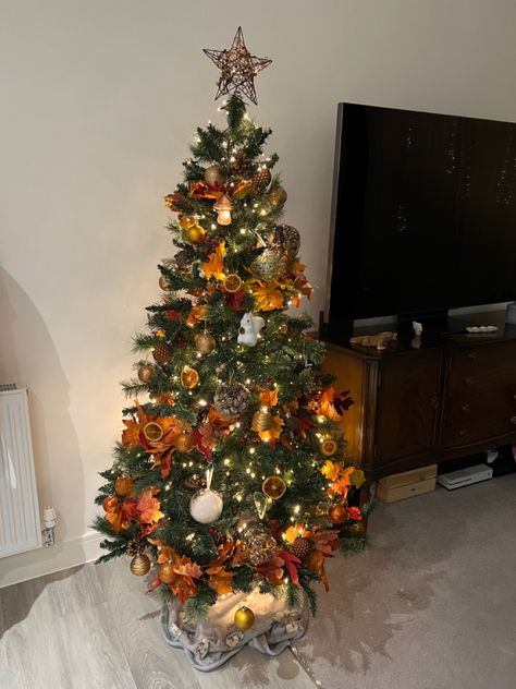 A dark green Christmas tree decorated with dehydrated orange slices, orange fall leaf garland, orange and brown baubles, acorns and red winter berries. On the top of the tree is a wicker star which also includes red winter berries. Throughout the whole tree are warm white lights giving a cozy vibe. Orange Christmas Decorations Color, Copper Orange Christmas Tree, Orange Gold Christmas Tree, Orange Themed Christmas Tree, Orange Theme Christmas Tree, Orange And Brown Christmas Decor, Orange And Red Christmas Tree, Autumnal Christmas Tree, Green And Orange Christmas Tree