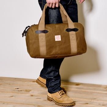 Filson Tin Cloth bags are made for traveling light and fast, with all of the weather resistance and durability that’s made our bags legendary. Whether as a gym bag or for a weekend at the cabin, this duffle is a go-to bag that’s built to last. The Tin Cloth Small Duffle is made with our iconic waxed canvas that’s protected foresters, sportsmen, and tradesmen from harsh weather, brush, and abrasion for more than a century. Thick cotton webbing handles are stitched down the sides of the bag for maximum strength. The carry grip is made with saddle-grade Bridle Leather that will mold to the shape of your hand for decades of comfortable carry. Nylon lines the interior for an added layer of protection for gear. The heavy-gauge metal zipper from YKK® is bult for years of unfailing service. Exteri Outdoor Rectangular Travel Bag With Top Carry Handle, Rectangular Outdoor Travel Bag With Top Carry Handle, Large Capacity Tote Duffle Bag For Outdoor, Outdoor Travel Tote Bag, Functional Waxed Canvas Bags For Overnight Trips, Outdoor Waxed Canvas Travel Bag With Luggage Sleeve, Waxed Canvas Bags With Luggage Sleeve For Outdoor Activities, Waxed Canvas Bags With Luggage Sleeve For Outdoor, Large Capacity Waxed Canvas Weekender Bag For Outdoor