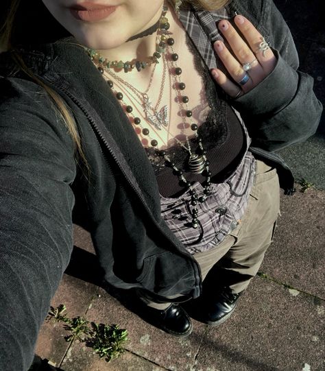 A mid-size person/girl wearing a thrifted tight grey waistcoat, a black lace tank top under it, wide dark olive green cargo pants, black platform dr. Martens and multiple crystal rings and bracelets. 	The person is also wearing multiple silver necklaces, one in form of a green crystal and another in form of a fairy  necklace, a black rosary-style bead necklace, a butterfly and a black lace choker. Grunge Green Pants Outfit, How To Style Green Cargo Pants Grunge, Fairygrunge Winter Outfits, Grunge Outfit Inspo Winter, Green Alternative Outfit, Fairygrunge Aesthetic Outfits, Green Cargo Pants Outfit Grunge, Forest Style Clothes, Forest Punk Aesthetic Outfits