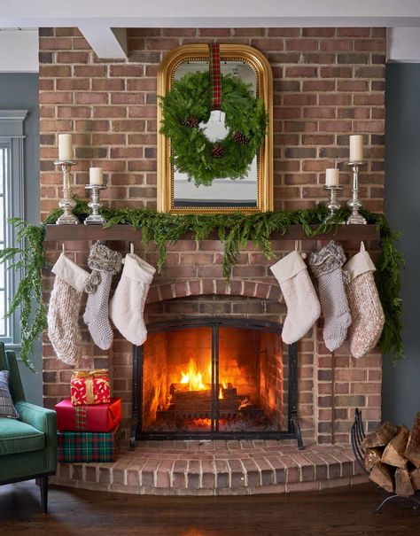 The wood-burning brick fireplace is original to this Illinois house. A large mirror above the mantel doubles as a gilt frame for the wreath. “This room is my favorite,” the homeowner says. “It’s so cozy." See our story for more photos! Christmas Brick Fireplace, Christmas Living Room Decor, Christmas Living Room, Midwest Living, Christmas Fireplace Decor, Farmhouse Fireplace, Christmas Decorations Living Room, Business Decor, Christmas Living Rooms