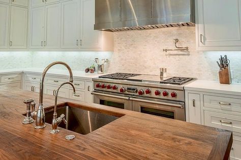 A butcher block kitchen island top holding an undermount stainless steel sink fitted with a gooseneck polished nickel faucet kit facing a Wolf dual range flanked by white shaker cabinets topped with white quartz countertops positioned against mosaic tumbled marble backsplash tiles holding a stainless steel hood above a polished nickel pot filler. Butcher Block Island Top, Butcher Block Countertops Island, Kitchen Island Top, Kitchen Sink Undermount, Butcher Block Kitchen Island, Sink Undermount, Kitchen Island Tops, Butcher Block Island Kitchen, Undermount Stainless Steel Sink