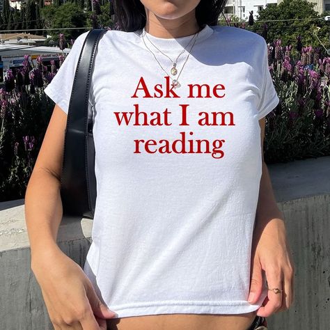 This Ask Me What I am Reading Baby Tee is the perfect addition to any book lover’s wardrobe. With its trendy aesthetic and comfortable fit, it's great for women of all ages. Show off your love for books while looking stylish and effortlessly cool. A ... #printwithsky #streetwear #trendytop #GraphicTee #BabyTee #pinterestinspired #londonstyle #lafashion #nycstyle #nycfashion #summeroutfit #90sfashion #90sbabes #pinterestgirl #whatiworetoday #dailyfashion Book Outfit Aesthetic, Book Tshirts Ideas, Lover Aestethic, Funny Graphic Tees For Women, Bookworm Outfits, Indie Shirts, Baby Tee Aesthetic, Reading Tshirt, Book Basket