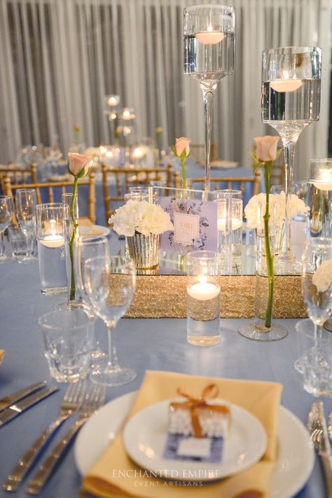 Under a canopy of fairylights this powder blue and gold wedding was the perfect style for this riverside location. Upon custom floor length satin linen, sat an array of floating candles, mercury gold vases filled with white blooms and bud vases, cradling rose stems to add a romantic whimsy to the dining space. Custom stationary kept the rose theme consistent with table numbers and individual thank you notes with an added bomboniere.  Youtube: www.youtube.com/watch?v=2-cqj3D3WAc Enchanted Emp... Wedding Centerpieces Blue, Gold Floating Candles, Wedding Centerpieces Diy Red, White Table Numbers, Centerpieces Blue, Summer Wedding Centerpieces, Blush Centerpiece, Gold Table Setting, Blue Wedding Centerpieces