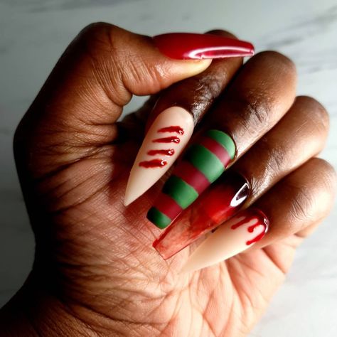 Red coffin and stiletto Halloween nails. Pointer and ring fingers are nude stiletto nails with bloody drip designs. Middle finger is a red and green Stripe nail that resembles Freddy Kreuger sweater. Ring finger resembles clear nail with blood staining the glass. Nails Red And Green, Green Halloween Nails, Nails 2022, Coffin Press On Nails, Striped Nails, Nails Red, Halloween Nail Designs, Nails Coffin, Cool Nail Art