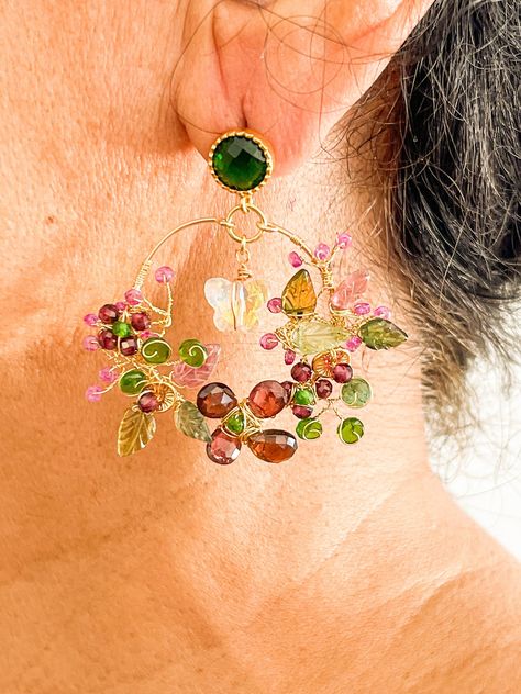 Large 14k gold filled artisan handmade vine hoop earrings with multi gemstones which I have wire wrapped into a bouquet of exquisite handmade flowers. This is a one of a kind and my unique design statement pair of earrings for boho women with emerald flat back studs, yellow crystal butterfly dangles and multi colored semi precious stone clusters of pink, green and yellow tourmaline carved leaves and green rondelles, red garnet faceted rondelles made into flower clusters and pink ruby gem unopene Vine Jewelry, Herkimer Diamond Jewelry, Flower Earrings Gold, Lucky Jewelry, Artisan Jewelry Handmade, Gemstone Hoop Earrings, Gemstone Earrings Gold, Pink Ruby, Tourmaline Earrings